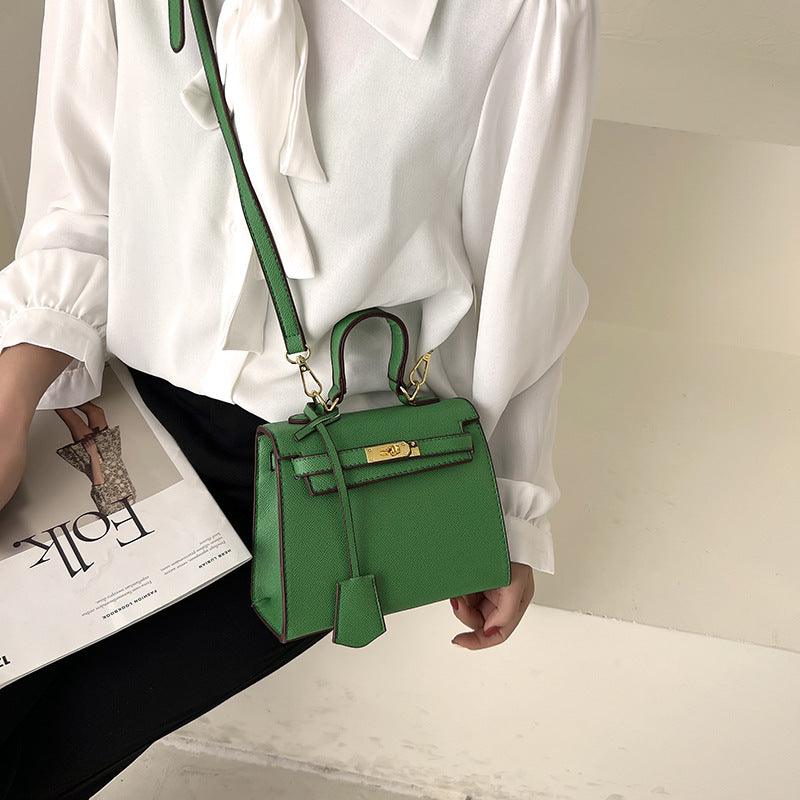 Green handbag held by a person wearing a white shirt, with a magazine underneath.