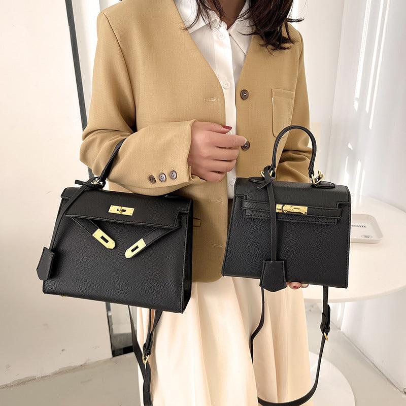 Person holding two black handbags with gold hardware against a neutral background