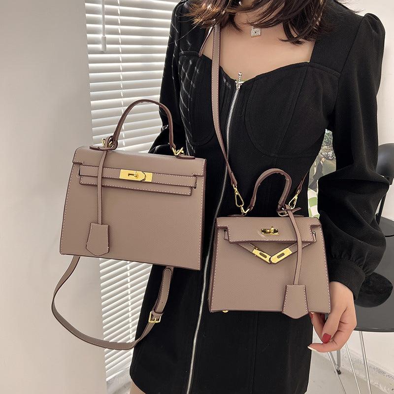 Person holding two beige handbags with gold hardware in an indoor setting.