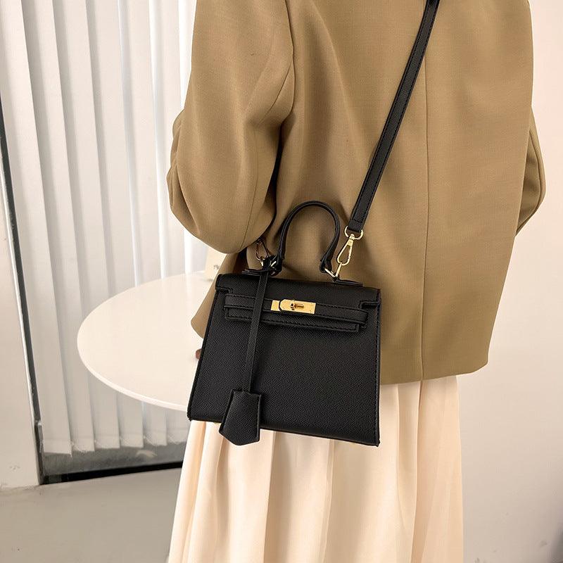 Person wearing a beige coat holding a black handbag with a gold clasp.