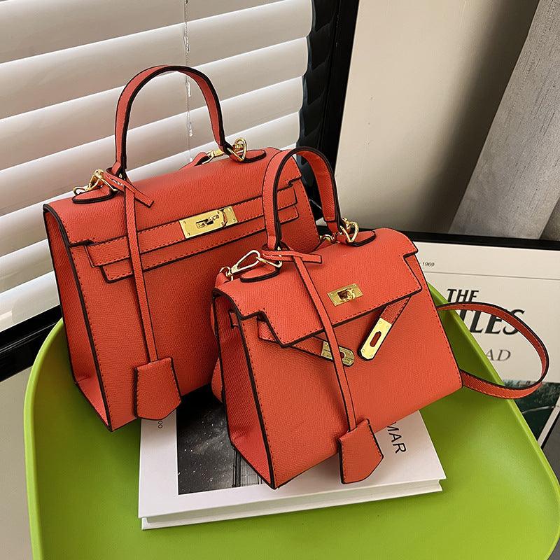 Two orange handbags with gold hardware on a green surface.